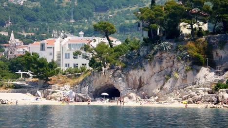 wide shot of tourists enjoying the beach near a cave in makarska croatia