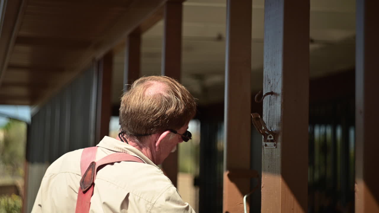 롤러 브러시로 파티오의 나무 기둥을 칠하는 노인의 뒷모습