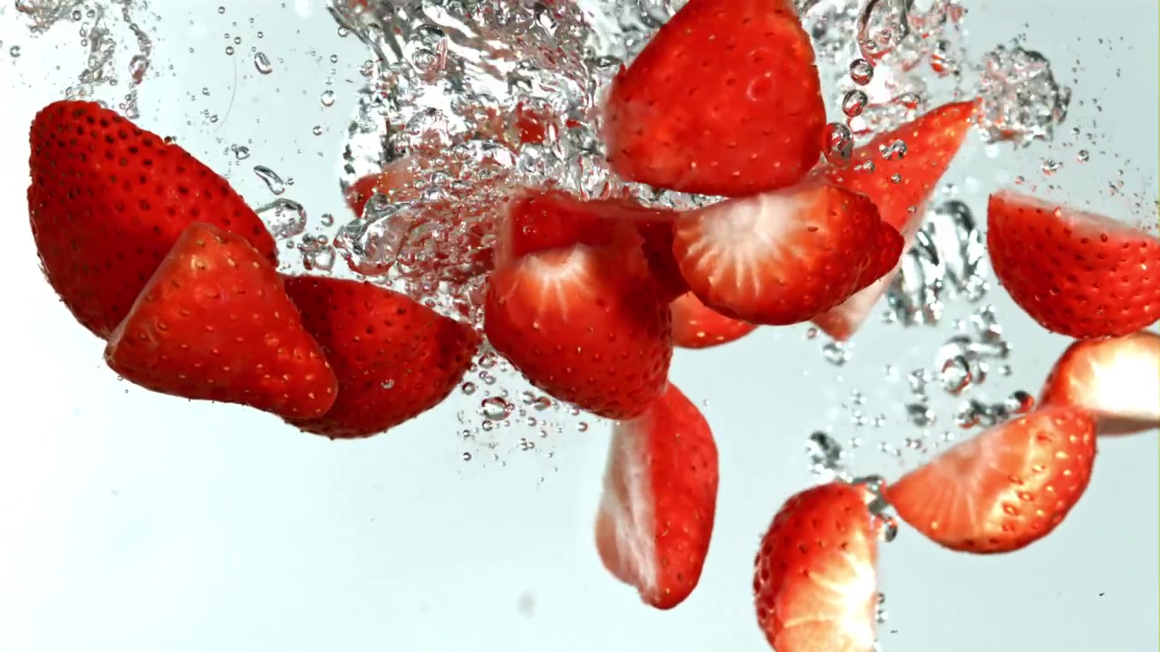 Fragole rosse fresche e fette che cadono in acqua limpida