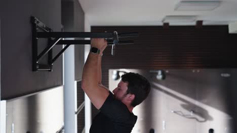 Bearded caucasian male do body weight pull ups at indoor gym facility