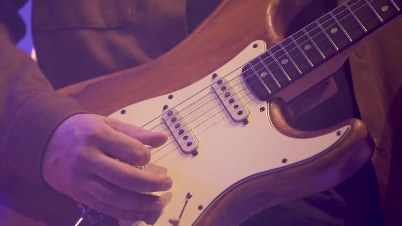 mano derecha del hombre de la banda tocando la guitarra eléctrica con púa lentamente, primer plano de las manos