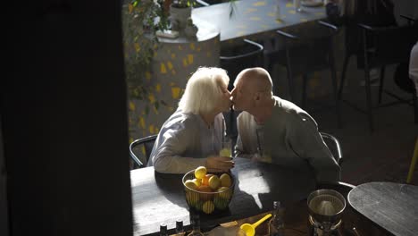 top view of a senior couple drinking limonade and kissing while they are sitting in a bar at sunset