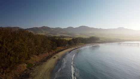 Beach-cove-with-pier-and-mountains-in-background