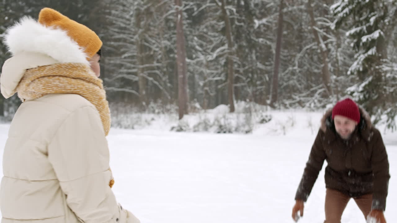 una pareja divirtiéndose jugando a las bolas de nieve en el bosque.