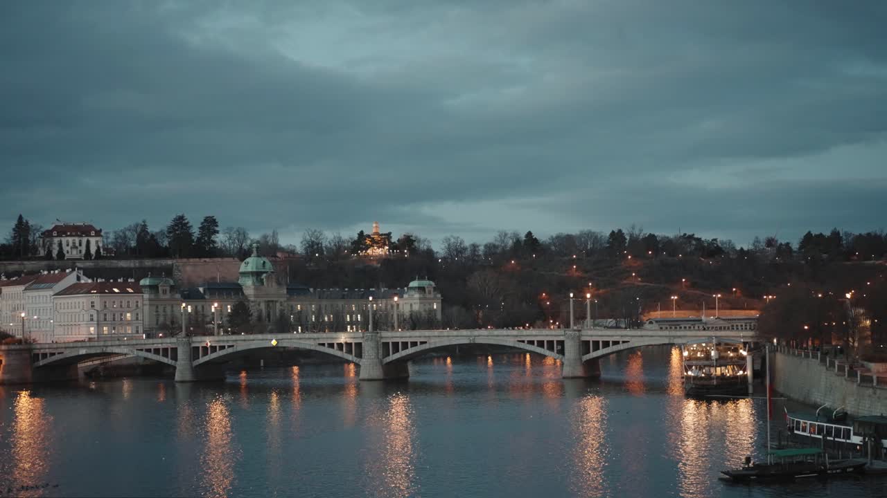 Ponte Mánes a Praga: Tranquilla vista sul fiume con skyline cittadino e silhouette del ponte.
