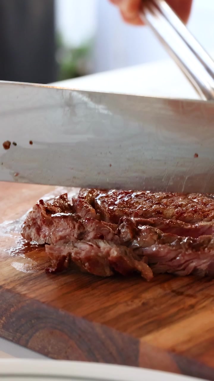 A chef slices a juicy beef steak on a wooden board in a well-lit kitchen setting