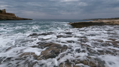 una toma cinematográfica de una profunda ola azul del océano salpicando violentamente sobre la costa rocosa en un día nublado