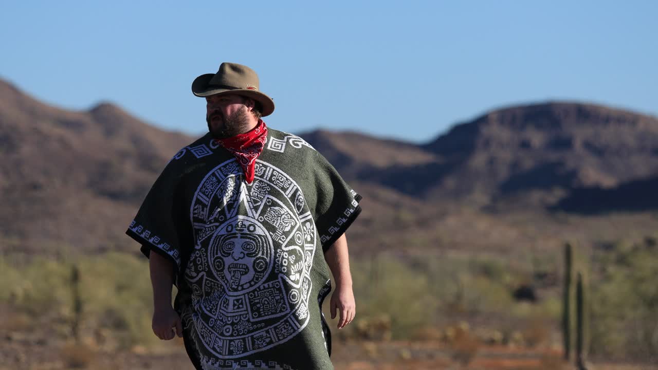 un hombre desesperado con un poncho, una bandana roja y un sombrero de vaquero en el desierto de sonora