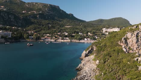 drone orbit past sloping rock cliff to reveal corfu greece bay and beach