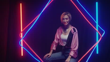 young woman with orange make up and short hair looking at camera and smiling in neon glowing tubes