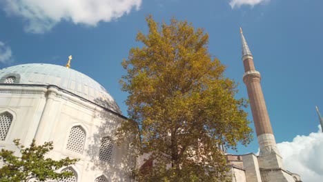 Tagsüber,-Bei-Teilweise-Bewölktem-Himmel,-Filmische-Zeitlupe,-Das-Minarett-Der-Hagia-Sophia-Moschee-Mit-Ein-Paar-Bäumen-Im-Vordergrund