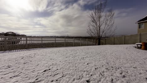 Time-lapse-of-a-suburban-backyard-with-a-thin-layer-of-snow-melting-as-spring-begins---tilt-down-time-lapse