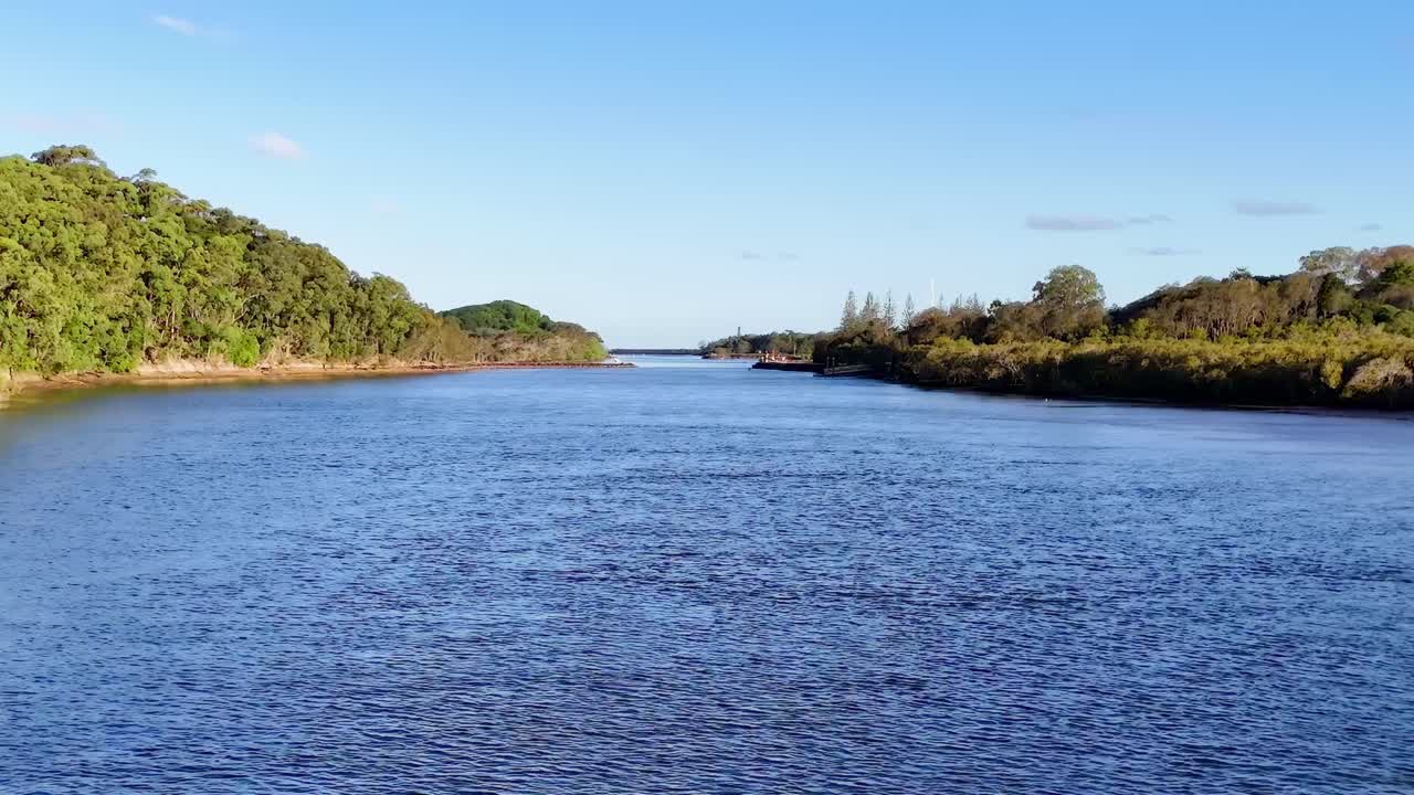 A tranquil river flows between lush green hills under a clear blue sky, creating a peaceful natural scene.