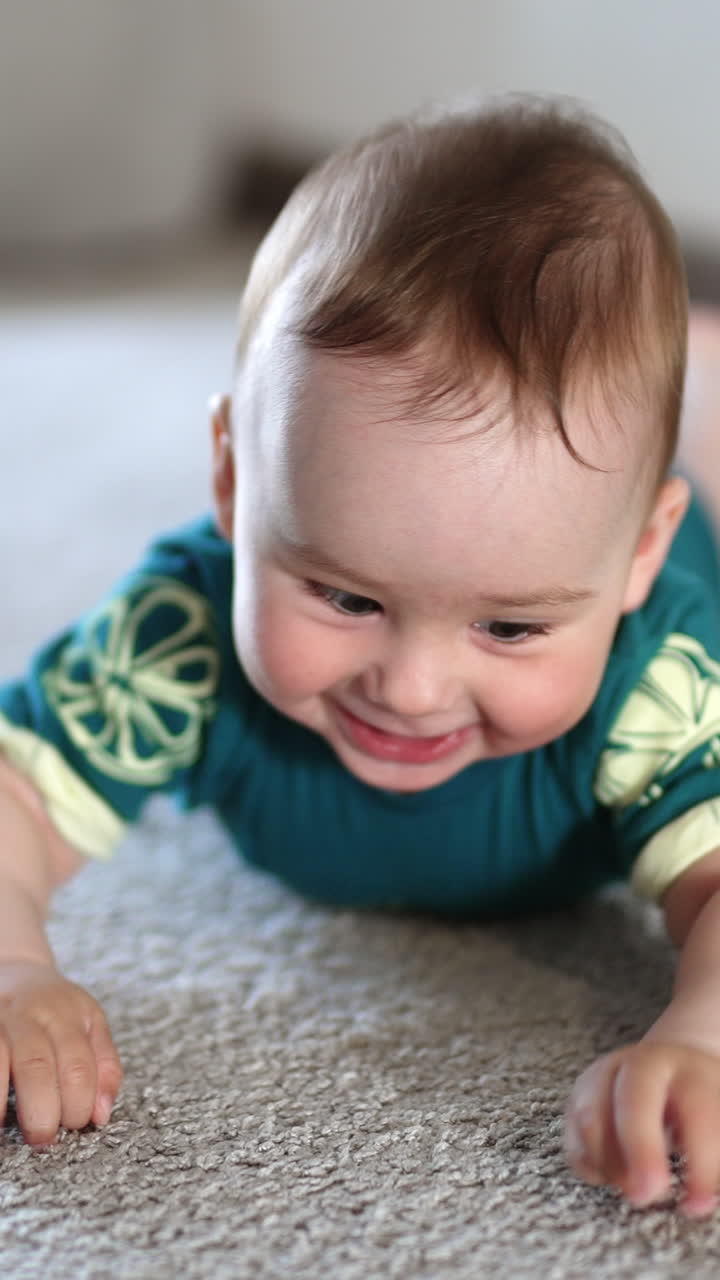 Cheerful happy Caucasian baby boy lies on belly smiling. Adorable child banging his limbs over the floor actively. Vertical video