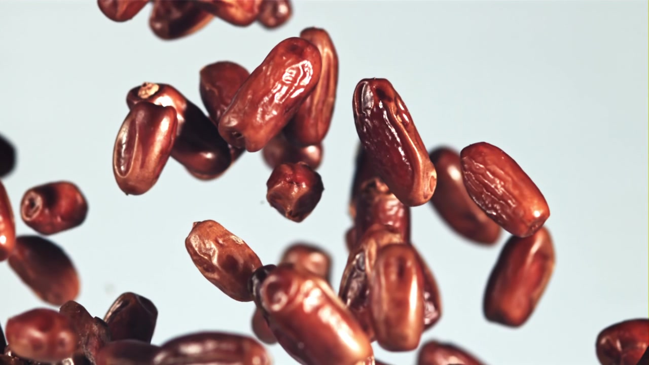 Dried Dates Falling and Floating in Slow Motion on a Light Background