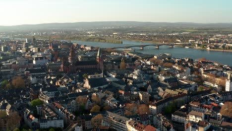 Círculo-Aéreo-De-Drones-Alrededor-De-La-Iglesia-Catedral-De-Mainz-En-Un-Cálido-Día-De-Primavera-Con-El-Río-Rin-Azul-En-La-Parte-De-Atrás