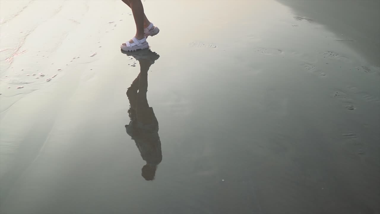 chica caminando sobre la arena mojada en la playa con sandalias