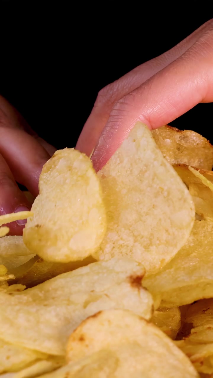 Mão joga e pega batatas fritas crocantes sob iluminação de estúdio brilhante contra um fundo preto.