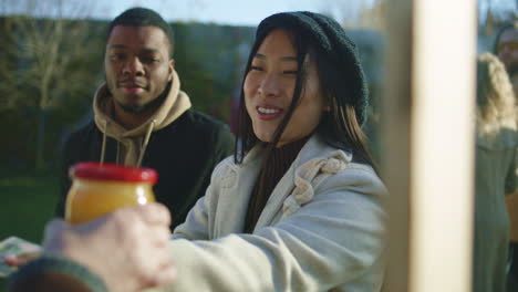 diverse couple buy honey at local farmers market diverse couple shopping at local farmers market asian woman pays for a jar of honey and puts it in eco bag people walking on background autumn fair on weekend outdoors vegetarian and organic food