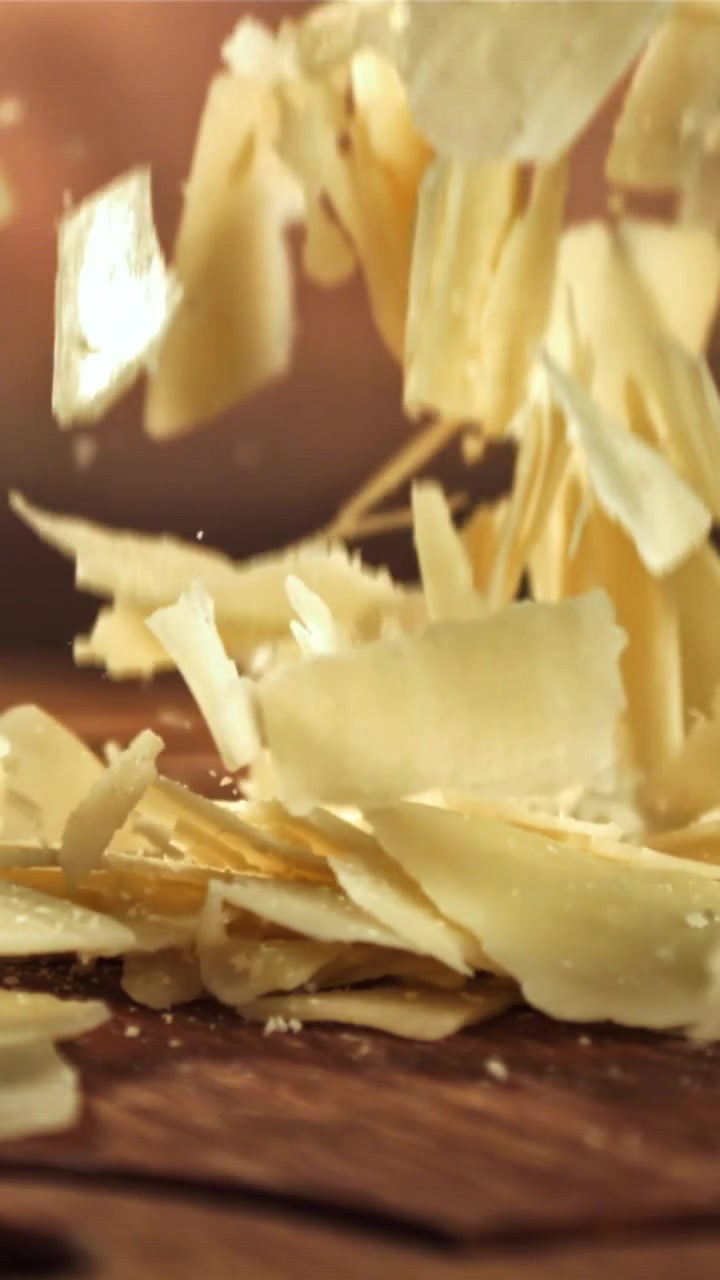 Copeaux de parmesan tombant au ralenti sur une surface en bois