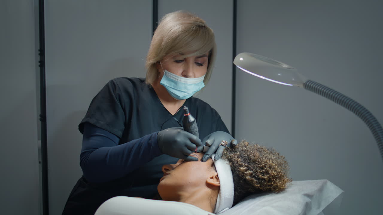 Donna che fa microblading alle sopracciglia in clinica con pigmento. Cosmetologa concentrata che trucca.