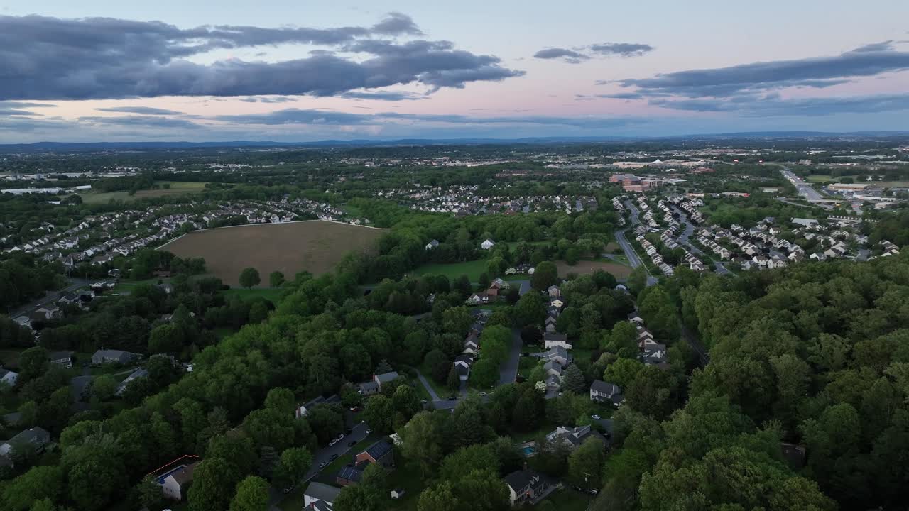 Quiet american suburb neighborhood with houses between green trees at dawn. Golden sunrise at sky in Pennsylvania. Aerial tilt up wide shot. Streets with one Family homes in United States.