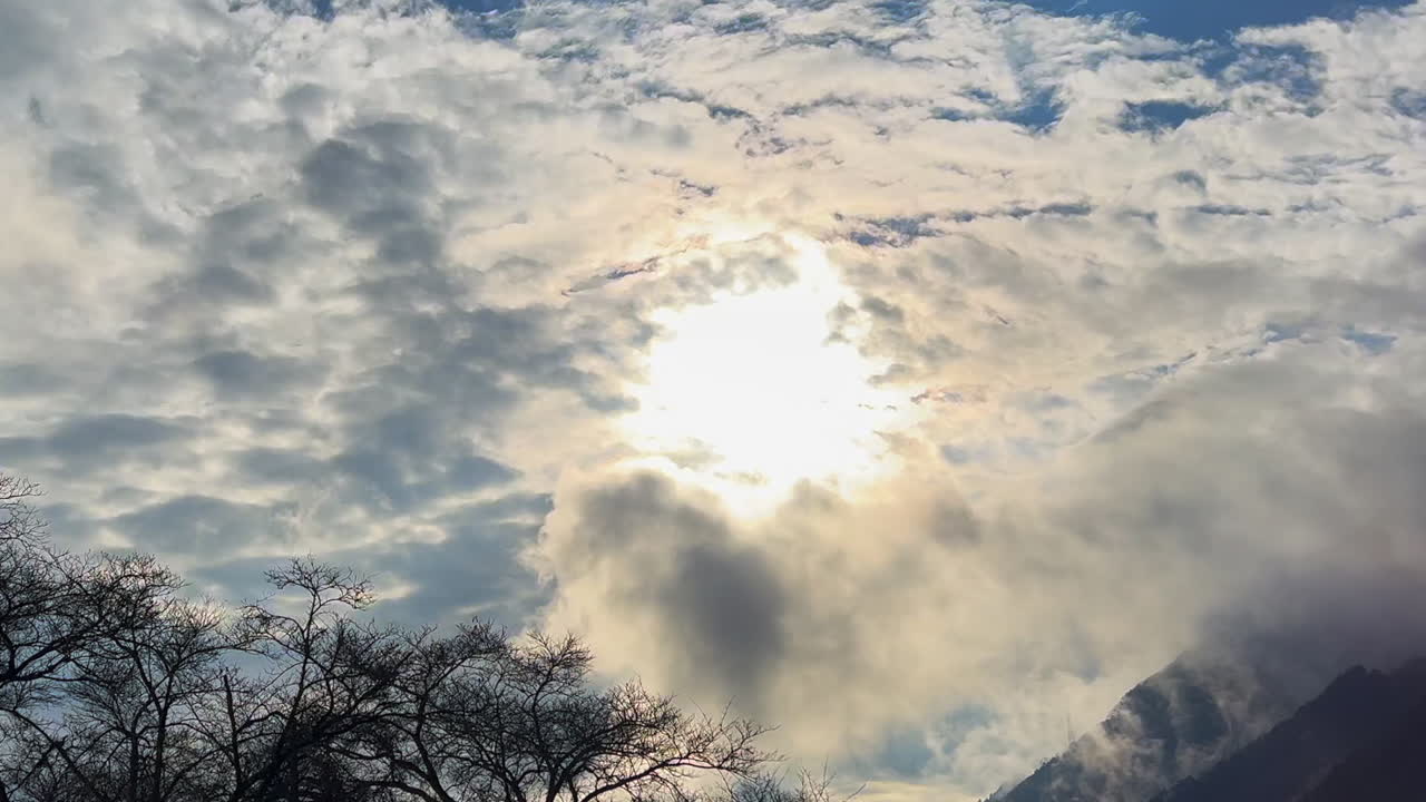 Nature background: Sun behind cloud in mountain sky, with tree tops