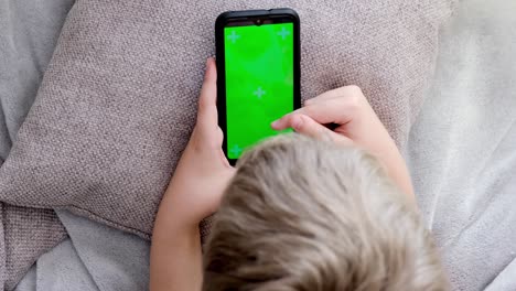 niño de 4k sosteniendo su teléfono inteligente con pantalla verde, desplazando la pantalla táctil