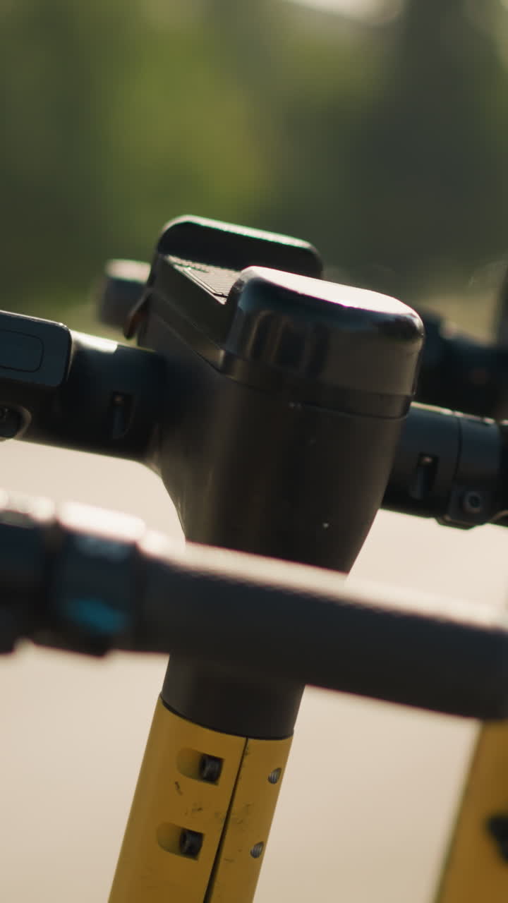 closeup scooter handlebar control module, textured grips and LED status ring on yellow stem with warm bokeh and blurred tree background, tactile button and display suggest technician inspection, user