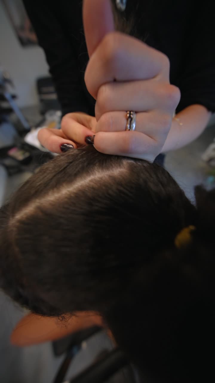 Parrucchiere professionista che intreccia i capelli scuri di una donna in salone