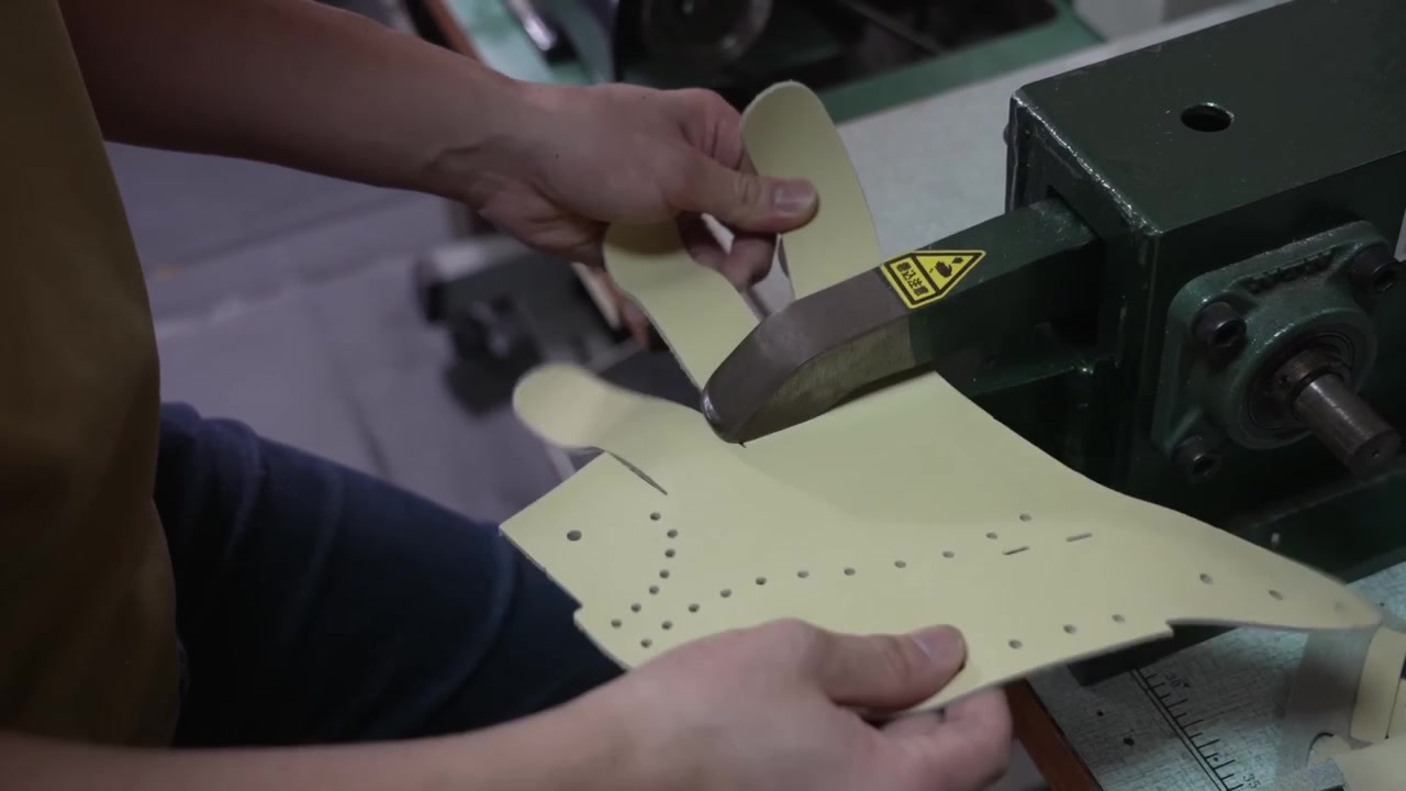 Hands inspecting a perforated leather glove panel with ventilation holes beside a bench vise