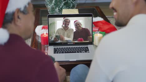 Padre-E-Hijo-Birraciales-Sonrientes-Usando-Una-Computadora-Portátil-Para-Una-Videollamada-Navideña-Con-Una-Familia-Feliz-En-La-Pantalla