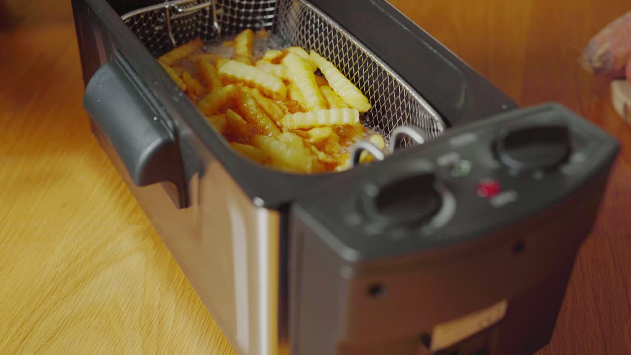 Kurv med pomfritter koger i elektrisk frituregryde, tilt op.