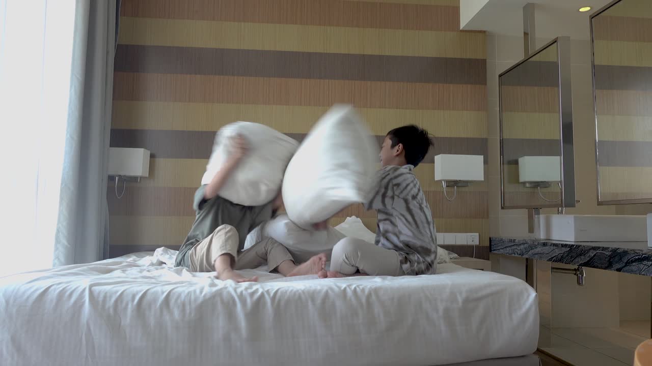Two Boys Having a Pillow Fight in a Hotel Room