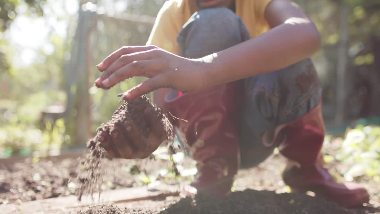 de manos de un niño afroamericano sosteniendo el suelo del jardín en un jardín soleado, cámara lenta