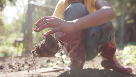 Hands-of-african-american-boy-holding-garden-soil-in-sunny-garden,-slow-motion