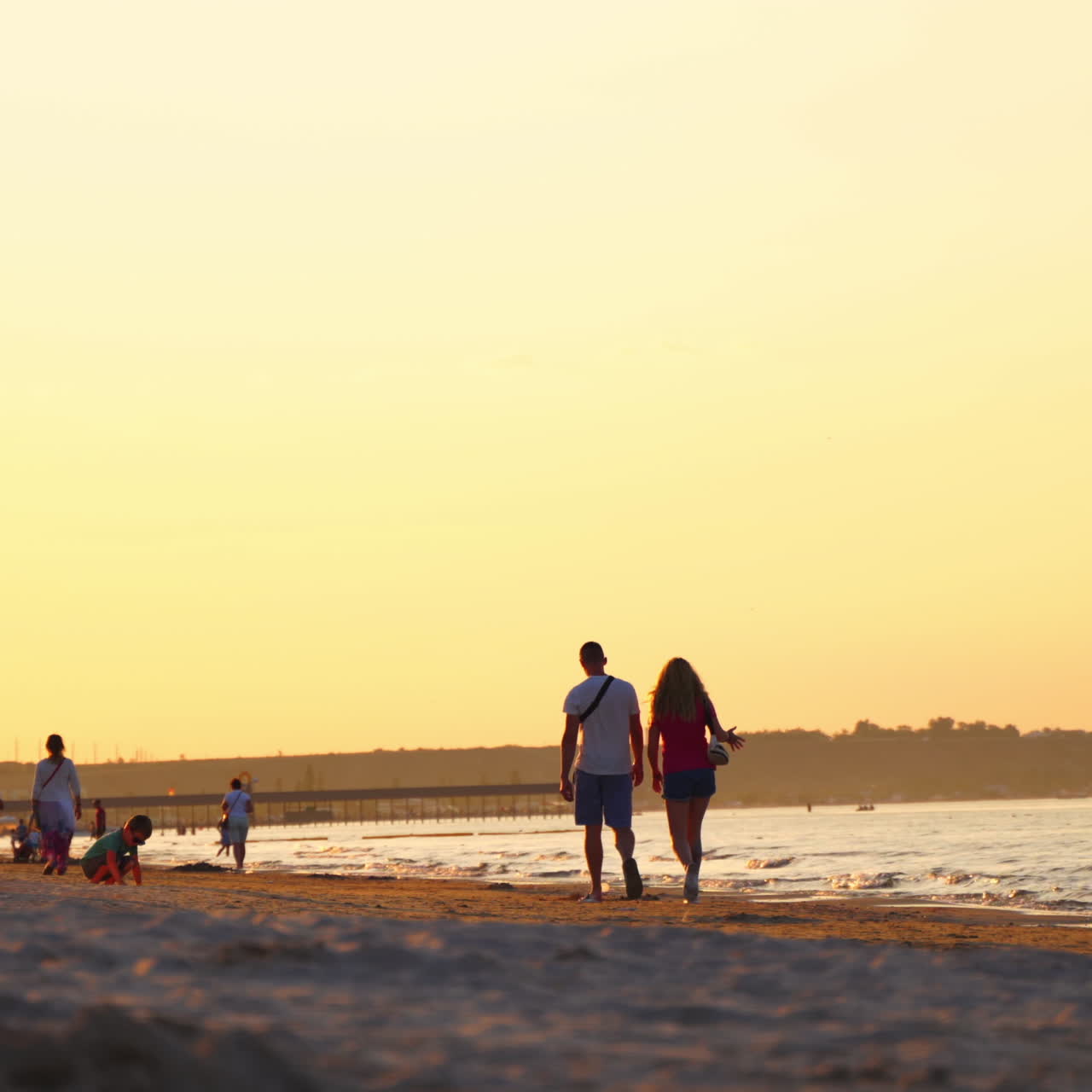 Back view of man and woman walking along beach at sunset. People go home from the seaside in the evening.