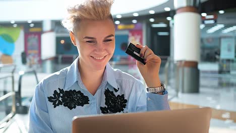 manos cerradas sosteniendo una tarjeta de crédito y usando una computadora portátil en el interior, compras en línea, mujer feliz.