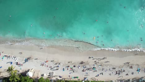 a drone starts with a beautiful view of crystal clear blue waters, sun, sand and families enjoying their travel vacation destinations and raises up to reveal even more of the beautiful environment