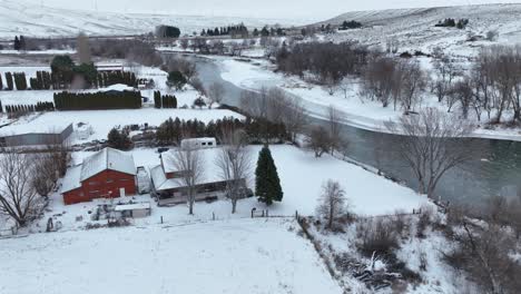 Toma-De-Drone-De-Una-Granja-Rural-Cubierta-De-Nieve-Que-Bordea-El-Río-Yakima.