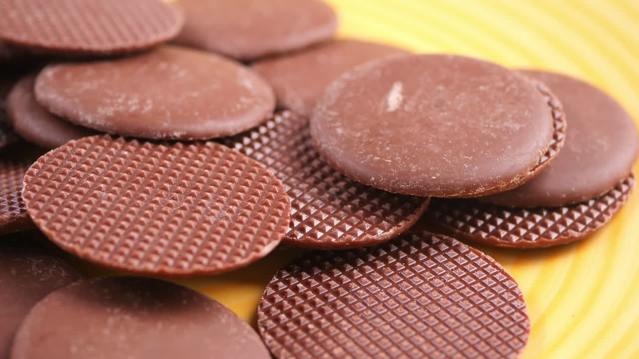 Primo piano di wafer al cioccolato che ruotano su un piatto giallo.