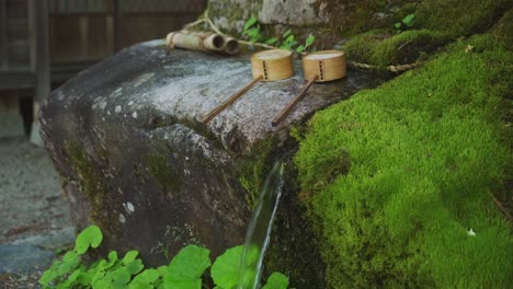 Wasser-Fließt-über-Moosbedeckten-Felsen,-Auf-Dem-Hölzerne-Schöpfkellen-Ruhen