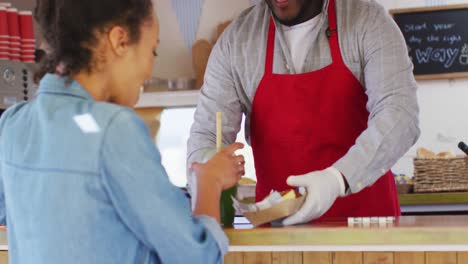 hombre afroamericano con delantal sirviendo y batido de papas fritas a una mujer en el camión de comida
