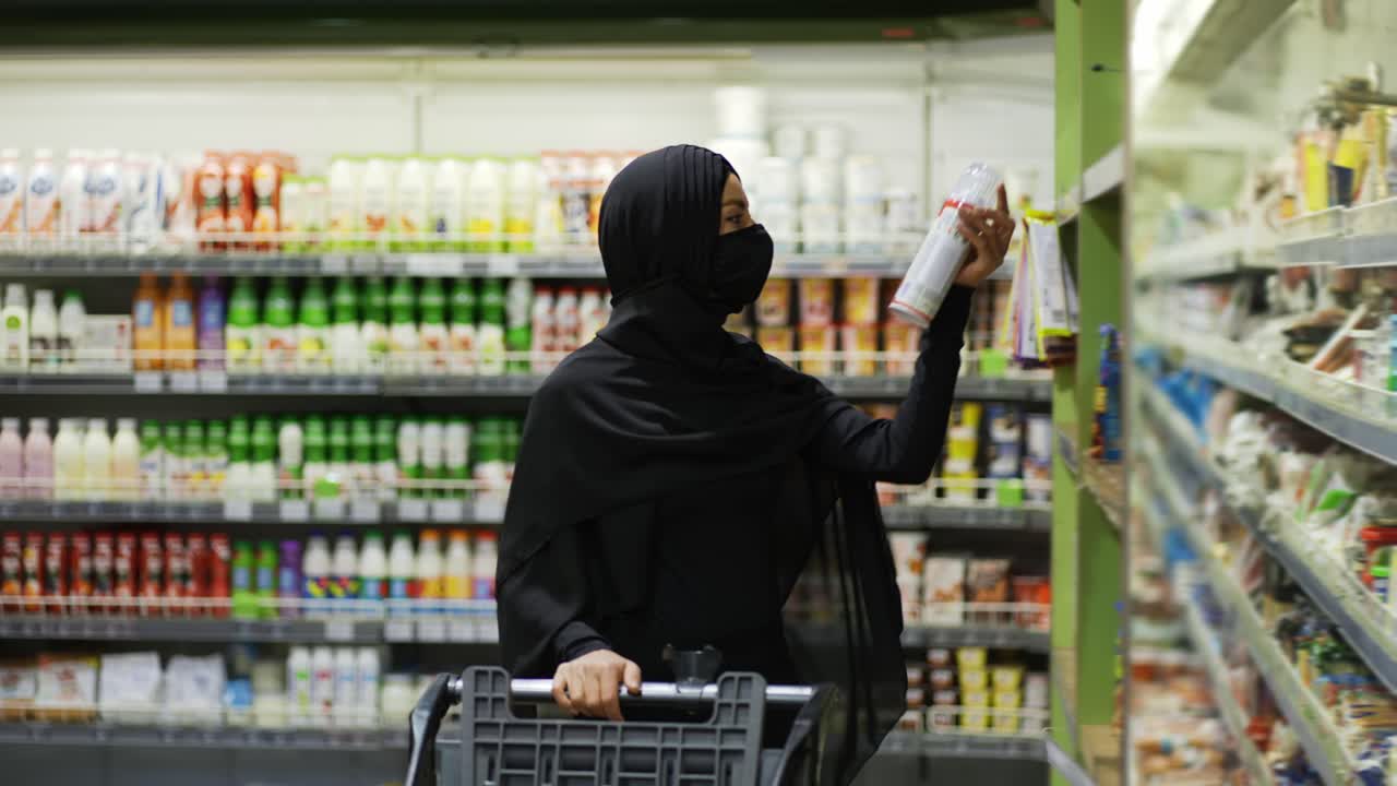 mujer con hijab y máscara protectora haciendo compras, toma el producto del estante, cámara lenta