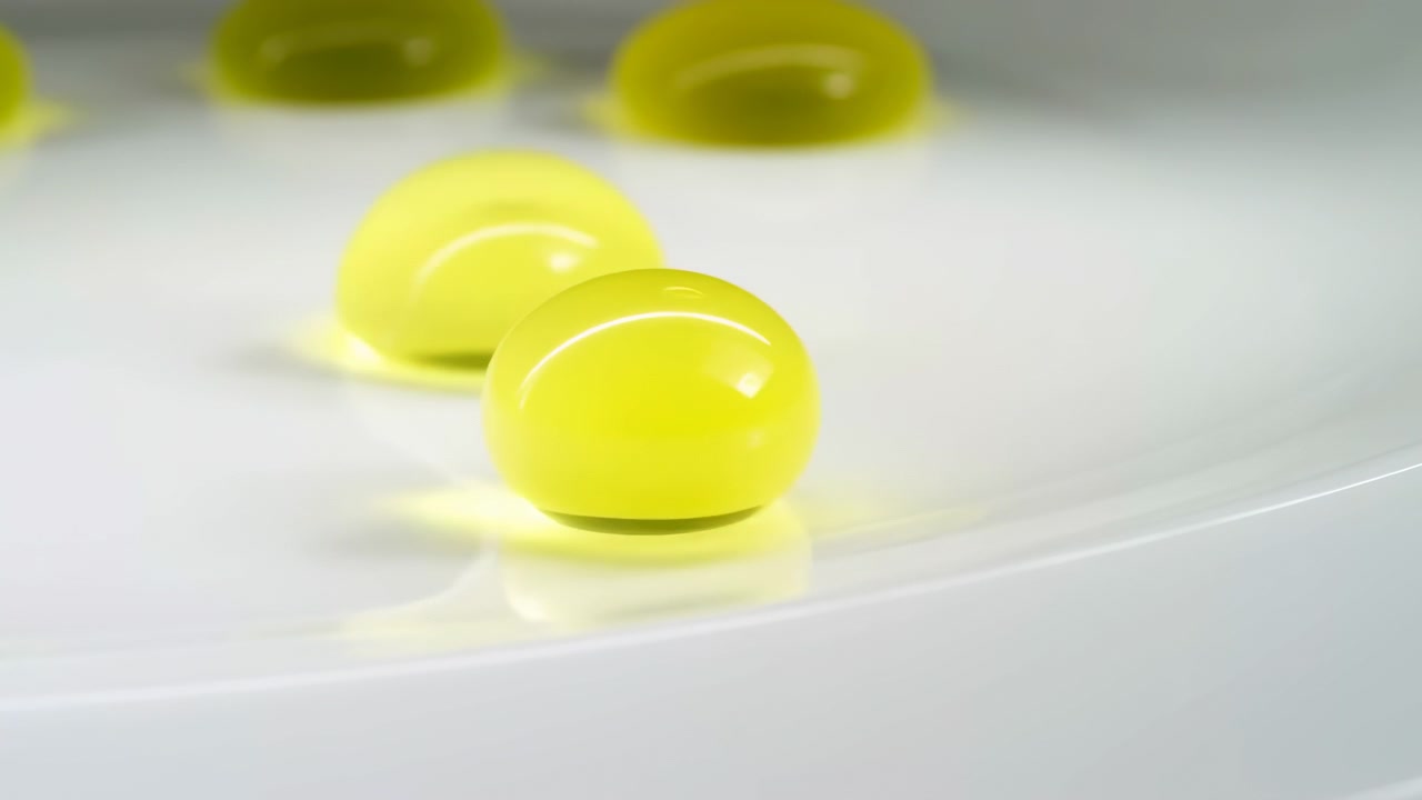 Scena ravvicinata in movimento che mostra sfere di gel lucide traslucide giallo-verdi che fluttuano, si toccano e si depositano su una superficie chiara riflettente con tenui riflessi, ombre delicate e uno stile pulito e minimale
