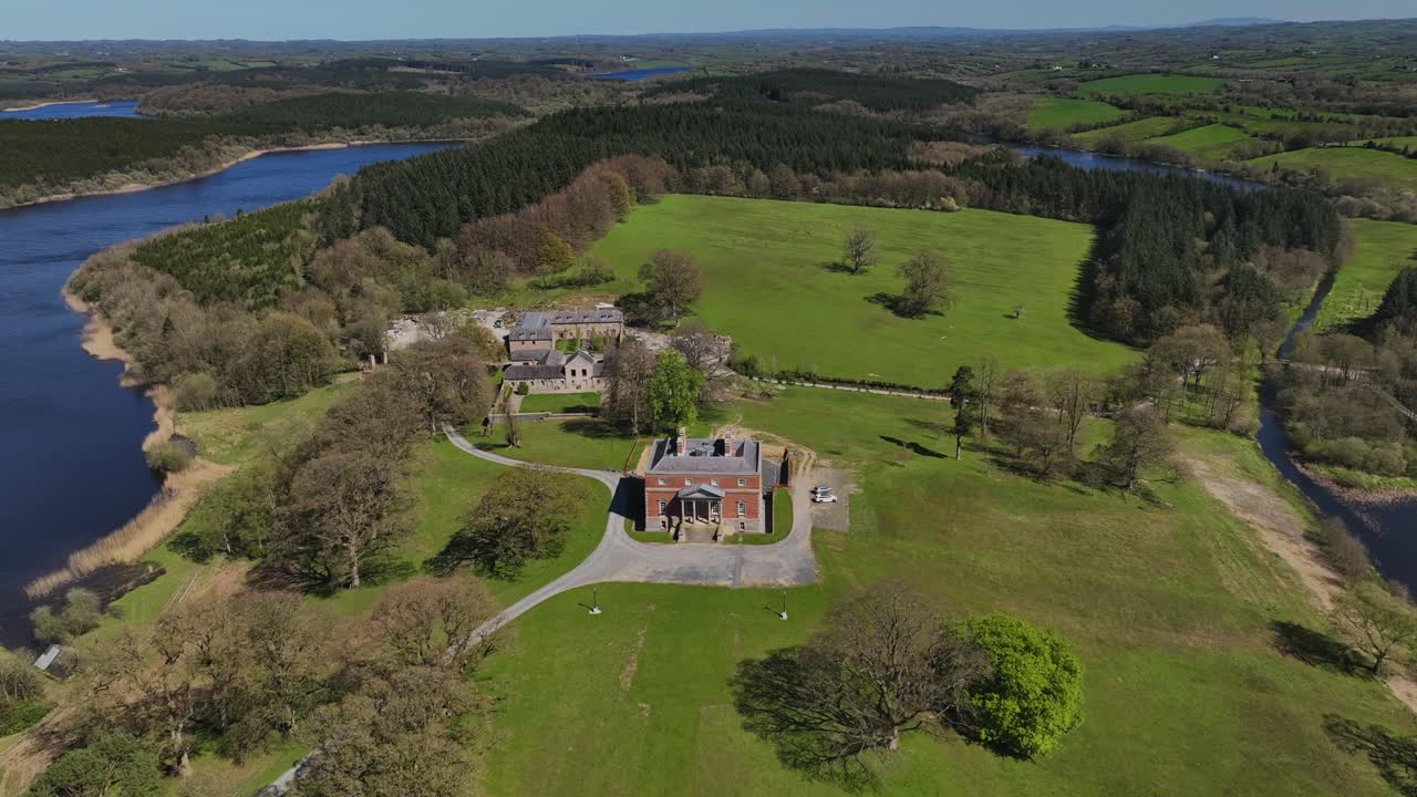 Bellamont House, County Cavan, Ireland, April 2023. Drone orbit counterclockwise over wide countryside, lush trees, historic charm under clear sunny blue sky.