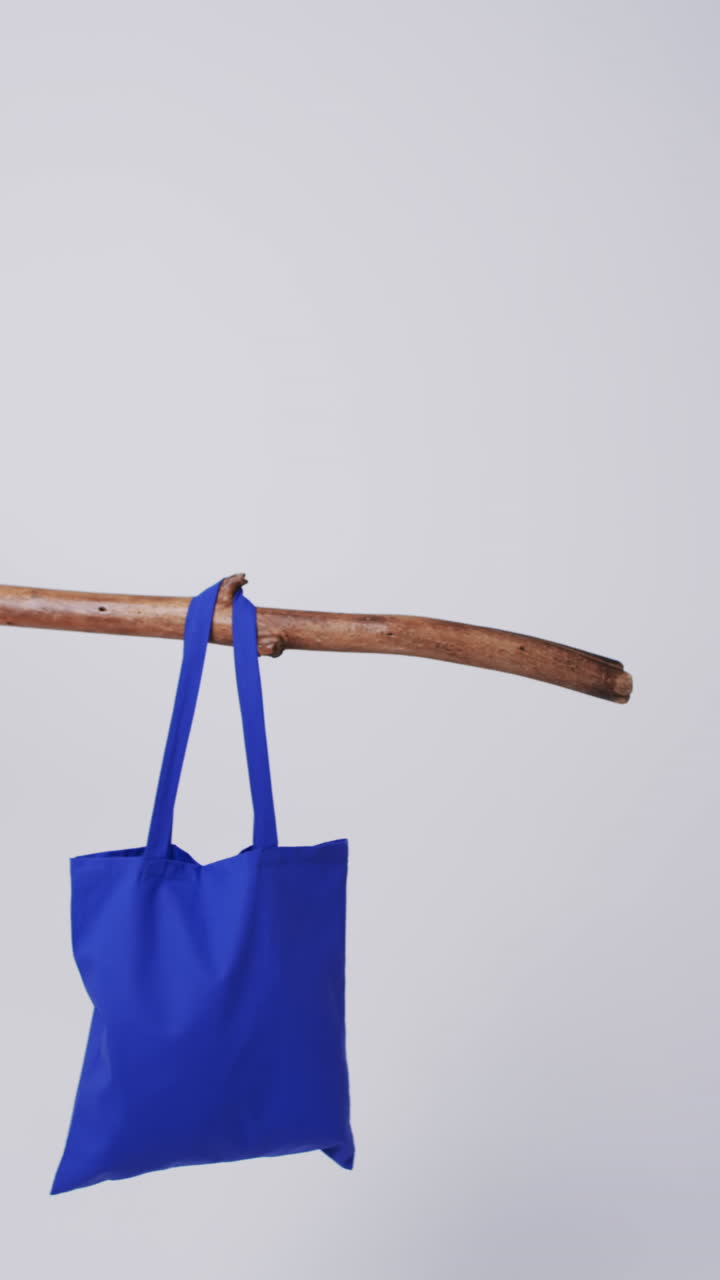 Vertical video of blue canvas bag hanging from branch with copy space on white background