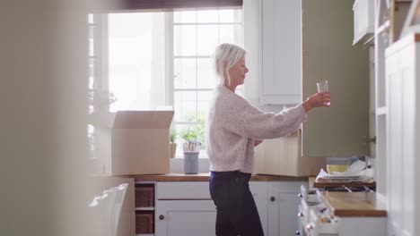 happy senior caucasian woman moving house, unpacking boxes in kitchen