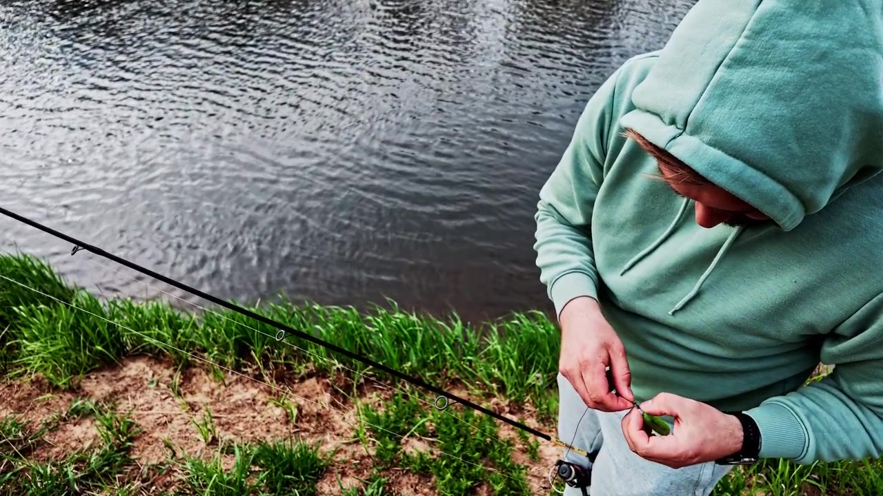 Fisherman rigging a soft plastic lure on a jig head for bass fishing on a riverbank
