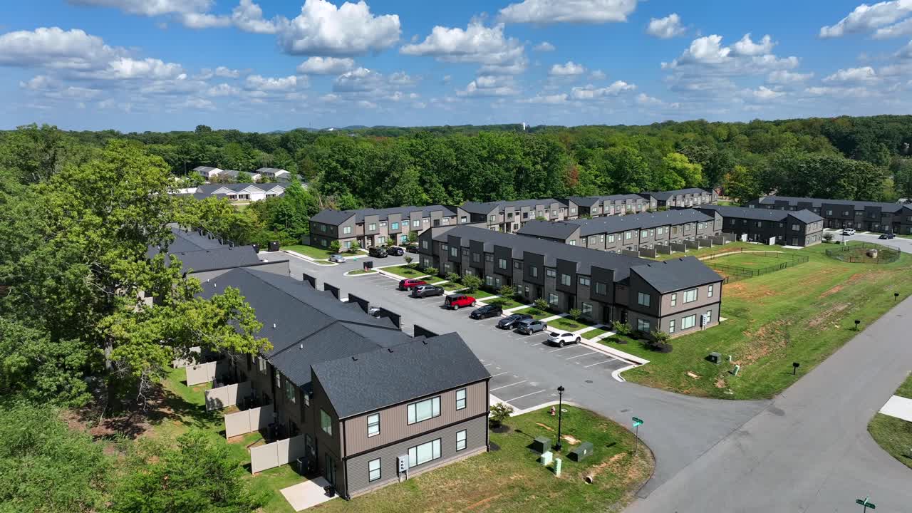 Modern architectural apartment houses in idyllic suburb of American town. Sunny summer day with parking cars and forest trees in background. Drone approaching shot. Row of design homes in USA.
